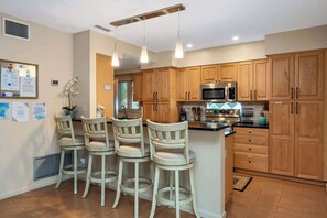 A kitchen with wooden cabinets, a stainless steel microwave, and a bar area with stools.