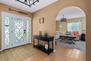 Un pasillo con una puerta decorativa, una consola negra y una sala de estar con sofá y mesa de centro.