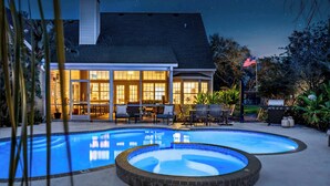 Una piscina con idromassaggio, area salotto esterna e una casa con ampie vetrate.