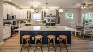 Una cucina moderna con mobili bianchi, elettrodomestici in acciaio inossidabile e un'isola centrale con sgabelli da bar.