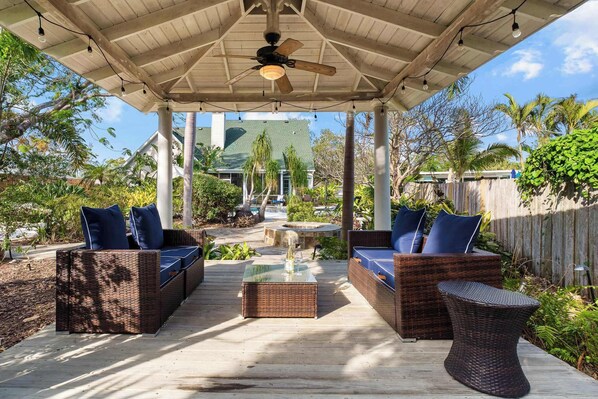 A covered outdoor seating area with wicker furniture and a ceiling fan.