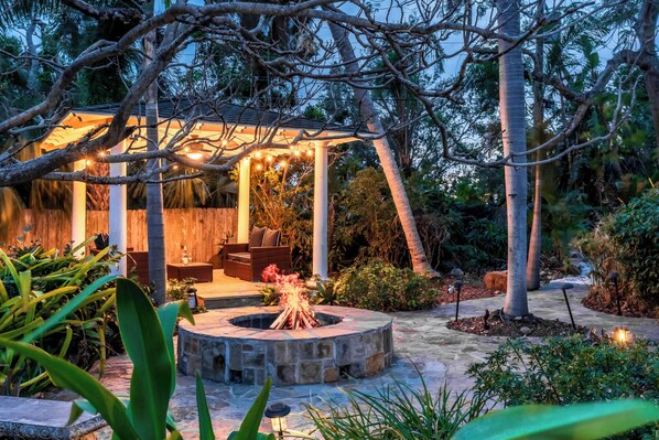 A patio area with a fire pit, outdoor seating, and a covered structure with string lights.