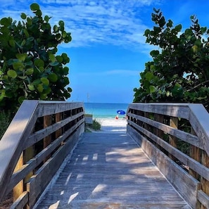 A wooden boardwalk leading to a beach with a clear sky.