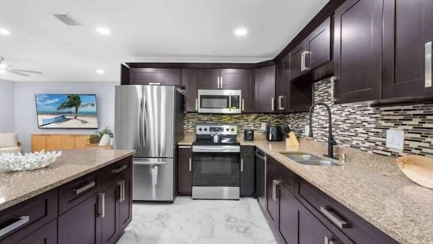 A modern kitchen with dark cabinets, stainless steel appliances, a granite countertop, and a backsplash with a mosaic tile pattern.