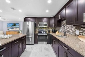 Uma cozinha moderna com armários escuros, eletrodomésticos de aço inoxidável, bancada de granito e painel com padrão de mosaico.