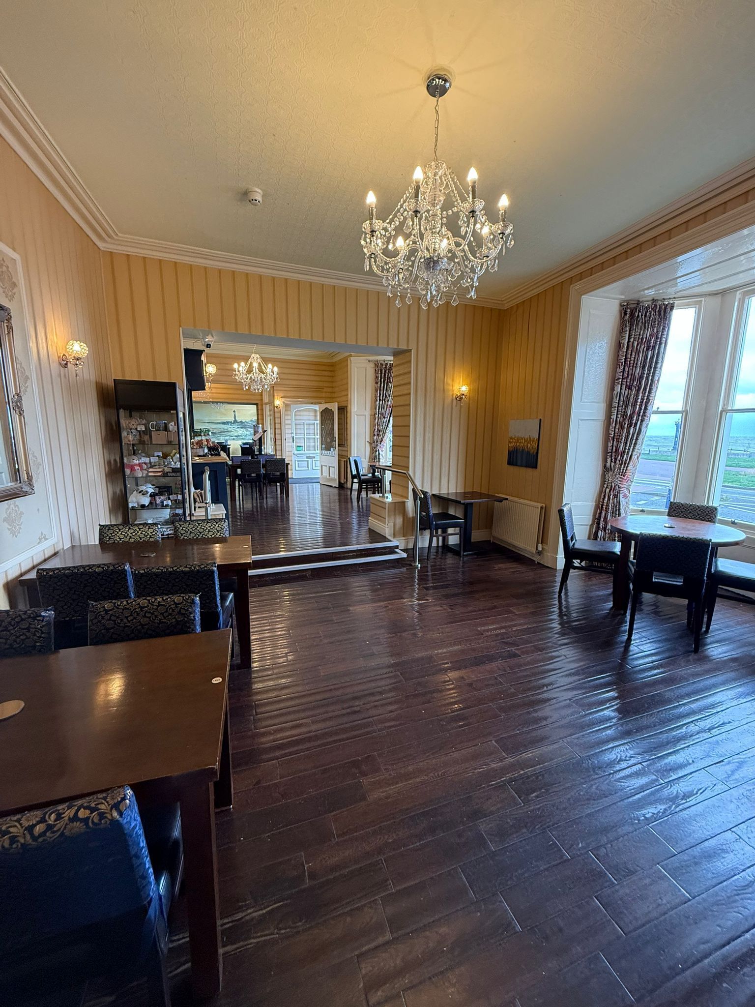 Une pièce spacieuse avec un grand lustre, un parquet en bois et une vue par la fenêtre.