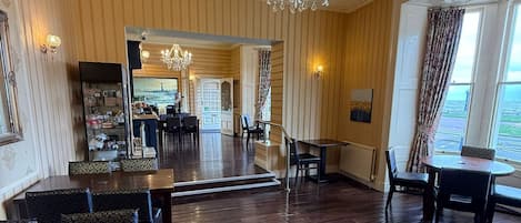 A spacious room with a large chandelier, wooden flooring, and a view through a window.