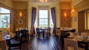 A dining area with wooden flooring, tables set for dining, and a bay window with curtains. - Baytree Hotel  (Llandudno)