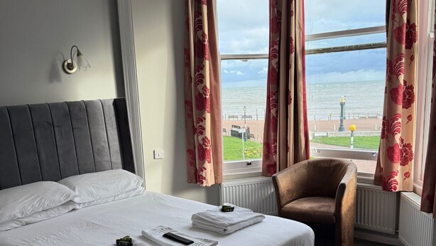 A hotel room with a bed, a chair, and a view of the sea. - Baytree Hotel  (Llandudno)