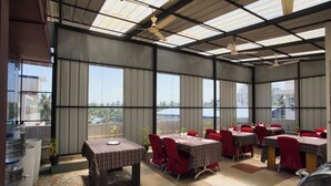 Un comedor interior con mesas y sillas, ventanas amplias y ventiladores de techo.