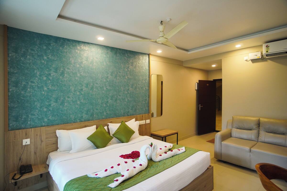A hotel room with a bed, a sofa, a ceiling fan, and an air conditioning unit.