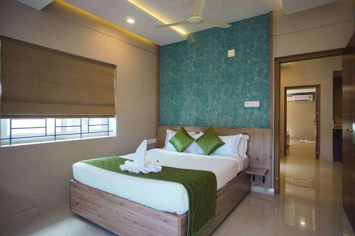 A modern hotel room with a large bed, a ceiling fan, and a view of the hallway.