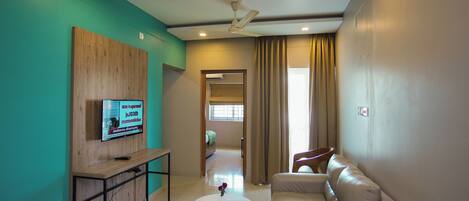A modern living room with a sofa, a coffee table, a TV mounted on a wooden panel, and a ceiling fan.