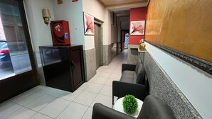 A hotel lobby with a reception desk, a fire extinguisher, and a hallway leading to other rooms. - Hostal Agarimo (Valle de Trapaga)