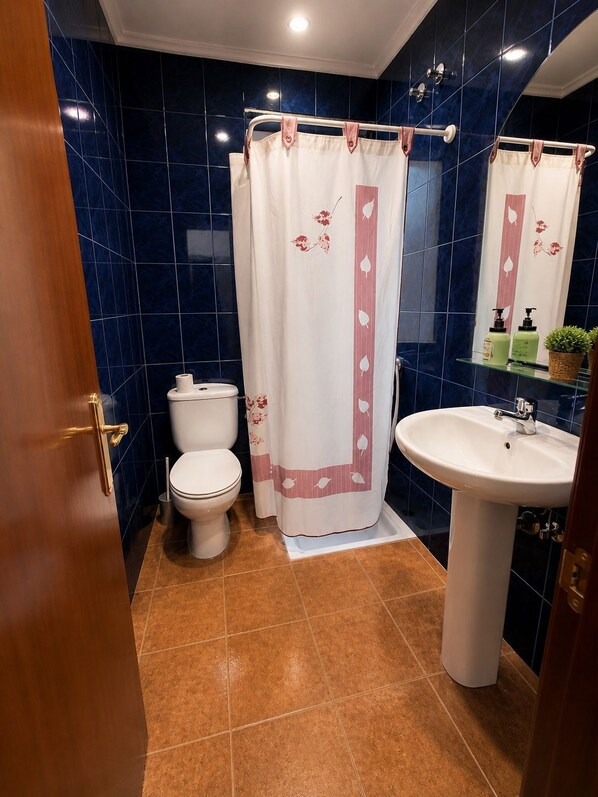 Un baño con inodoro blanco, lavabo y cortina de ducha con motivos florales.