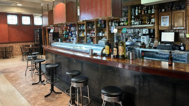 A bar area with stools, a counter with bottles, and a cash register. - Hostal Agarimo (Valle de Trapaga)