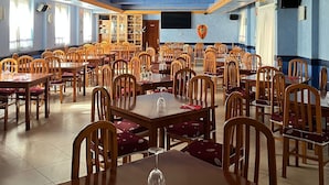A spacious dining area with multiple tables and chairs, a large window, and a ceiling vent. - Hostal Agarimo (Valle de Trapaga)