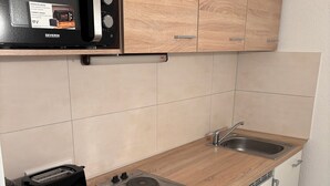 A compact kitchen with a microwave, toaster, and two electric stoves on a wooden countertop. - Cozy vacation apartment at Ammelshain Castle (Naunhof)