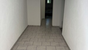 A hallway with tiled flooring and white walls, leading to a room with a bed. - Cozy vacation apartment at Ammelshain Castle (Naunhof)