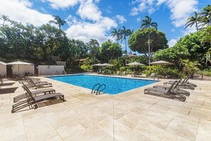 A swimming pool with lounge chairs and umbrellas, surrounded by palm trees and greenery.