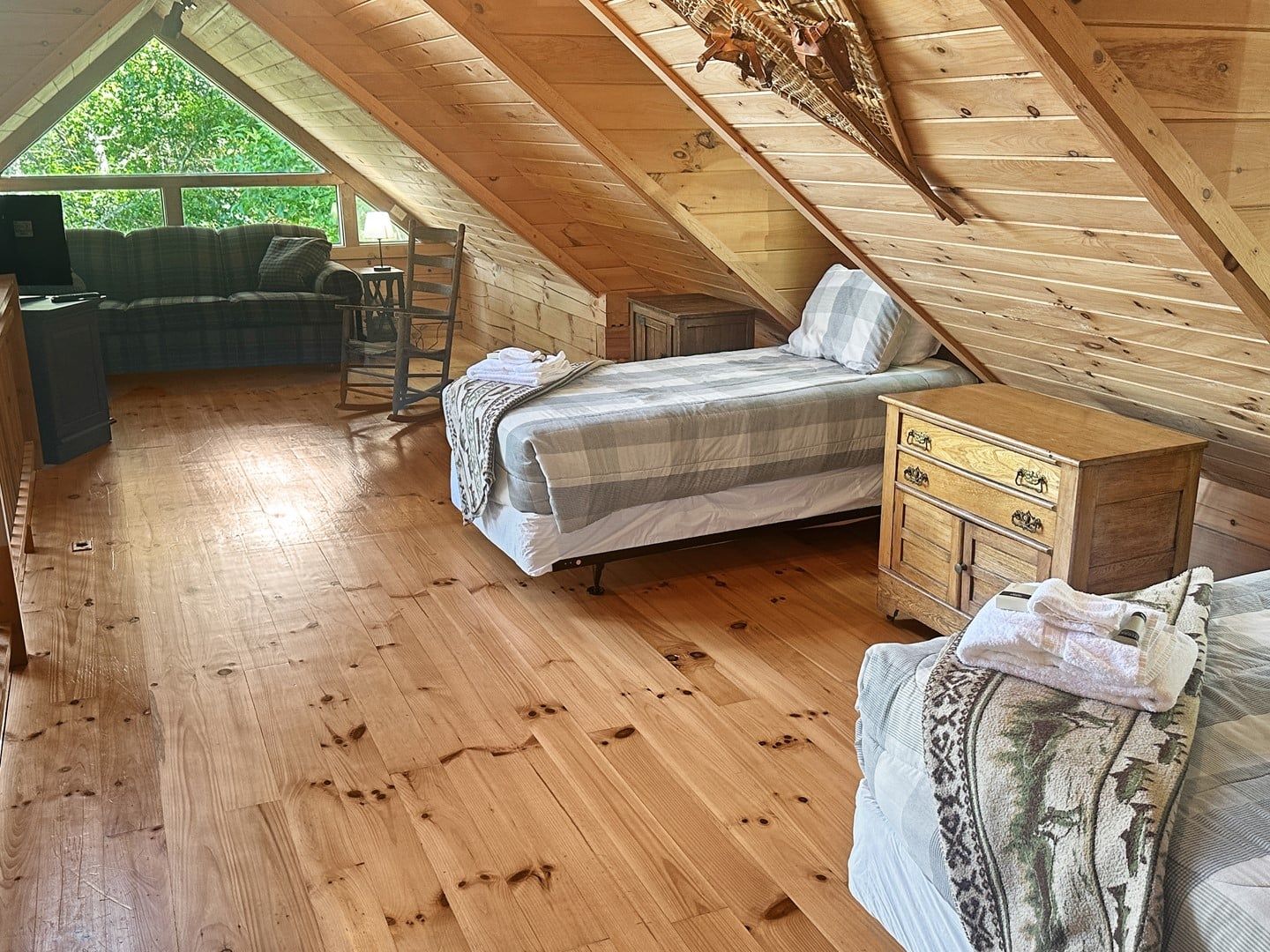 A cozy attic bedroom with a wooden floor, a bed, a dresser, and a desk area.