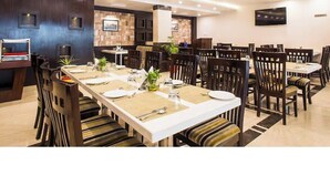 A modern dining area with multiple tables and chairs, ceiling vents, and a brick accent wall. - Hotel The Westinn (Varanasi)
