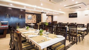 A modern dining area with multiple tables and chairs, ceiling vents, and a brick accent wall. - Hotel The Westinn (Varanasi)