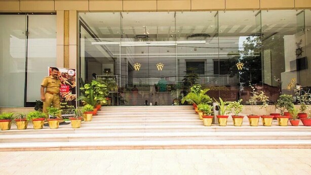 A modern hotel entrance with glass doors, potted plants, and a security guard. - Hotel The Westinn (Varanasi)