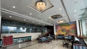 A hotel lobby with a large mural, seating areas, and a staircase leading to upper floors. - Hotel The Westinn (Varanasi)
