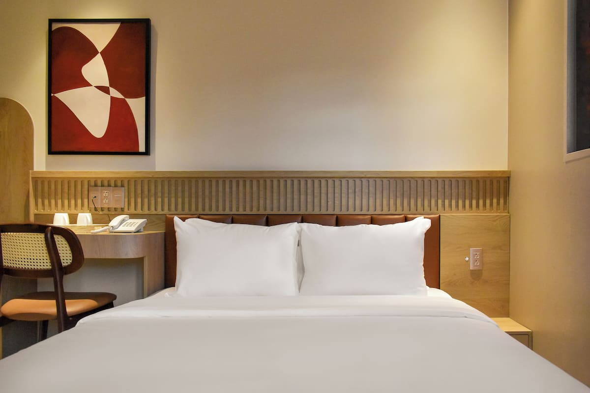 Ein Hotelzimmer mit einem Bett, einem Schreibtisch, einem Stuhl und einem an der Wand befestigten Telefon.