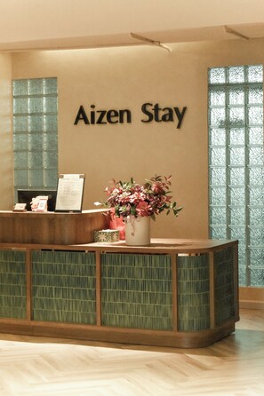 A reception desk with a sign that reads "Aizen Stay" and a floral arrangement on the counter. - Aizen Stay - District 1 (Ho Chi Minh City)