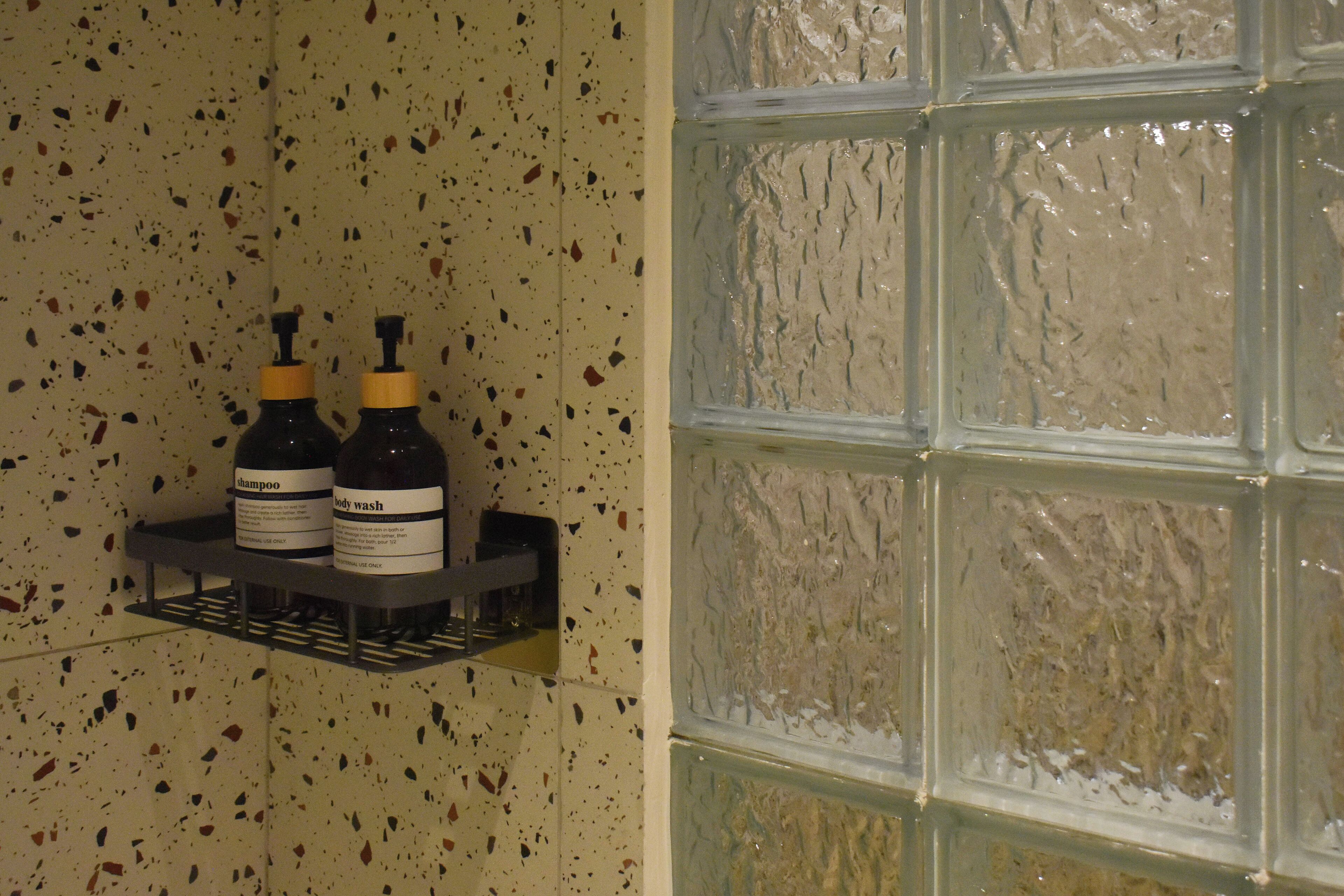 Un bagno con parete screziata e finestra con vetro satinato. Su uno scaffale, due flaconi di shampoo e bagnoschiuma.