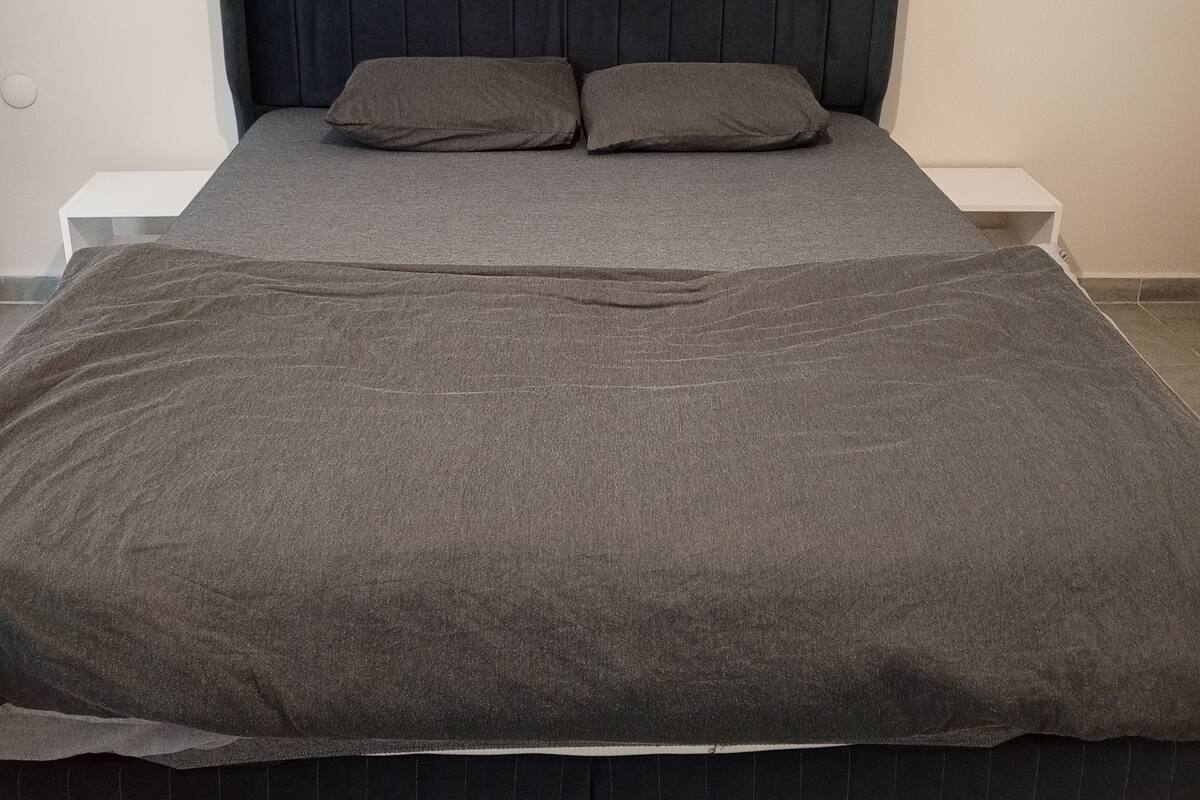 A bed with a dark headboard, two pillows, and a grey blanket.