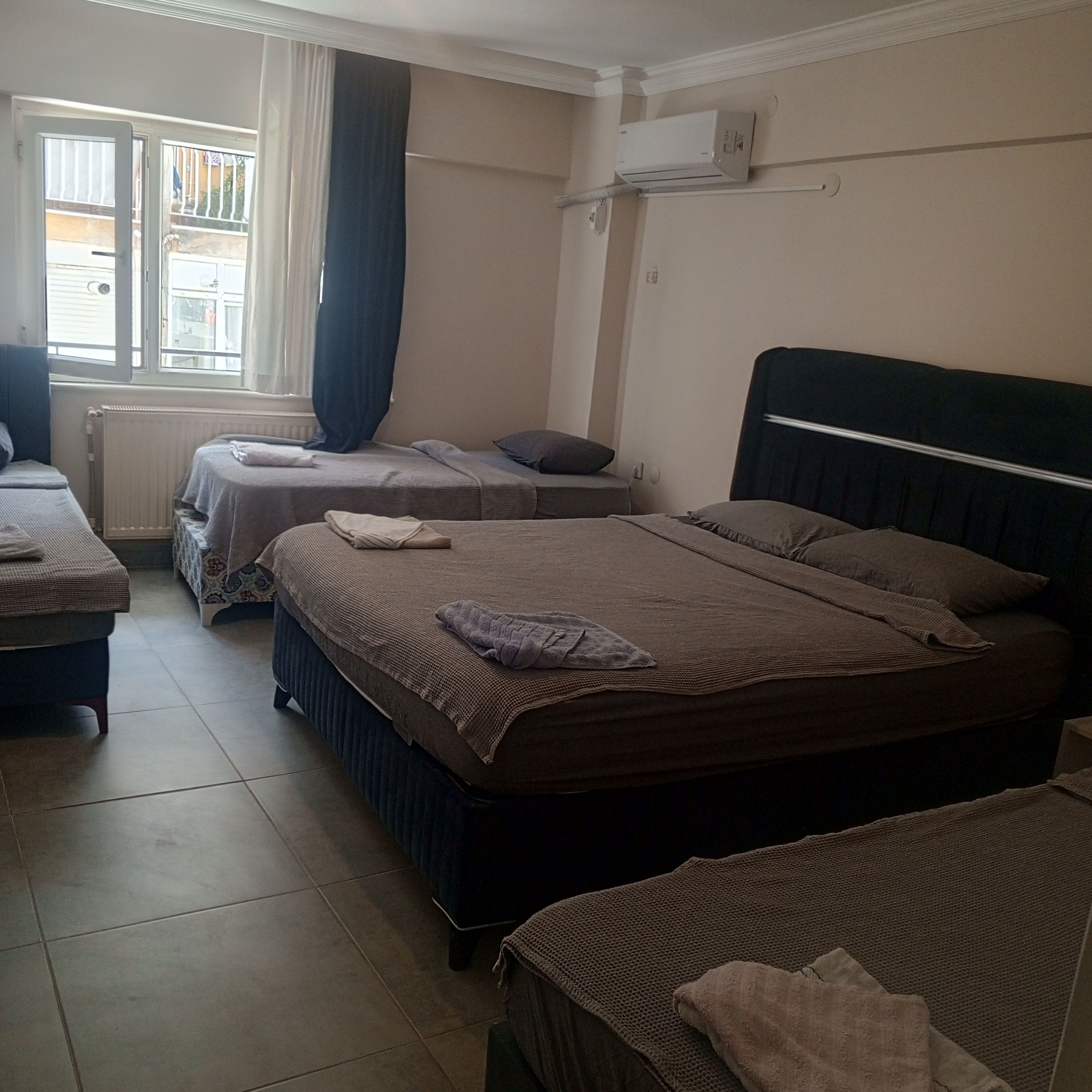Una habitación de hotel con dos camas, una ventana con cortinas, un equipo de aire acondicionado y un radiador.