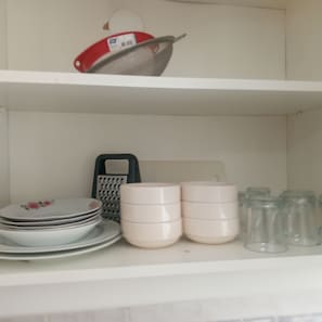 A kitchen shelf with stacked plates, a colander, a grater, and several glass jars. - Anka 1 (Aydın)