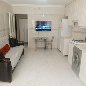 A compact living space with a sofa, a dining table with chairs, a washing machine, and a television mounted on the wall. - Anka 1 (Aydın)