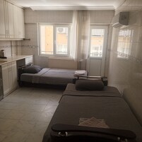 A compact room with two single beds, a small kitchenette, and a window providing natural light.