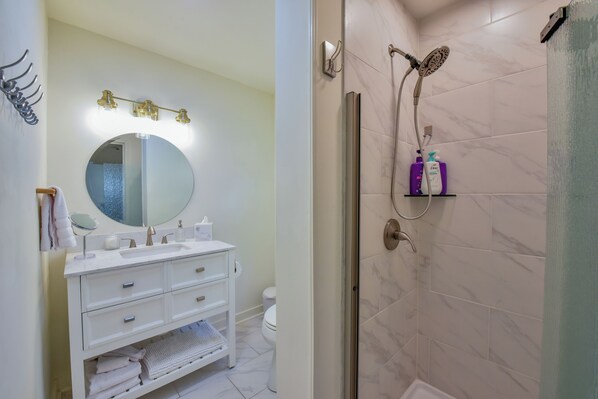 Un baño moderno con un tocador blanco, un espejo redondo y una ducha con mampara de vidrio.
