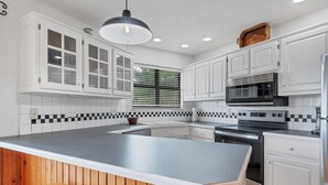 A modern kitchen with white cabinets, a black countertop, and a wooden island with a stool. - Everview 3 BR 3 BATH Spectacular Mountain Views Firepit, Wi-Fi, Free Pool Access (Townsend)
