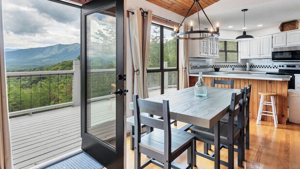 A modern kitchen with a large island, wooden ceiling, and a view of mountains through a sliding door. - Everview 3 BR 3 BATH Spectacular Mountain Views Firepit, Wi-Fi, Free Pool Access (Townsend)