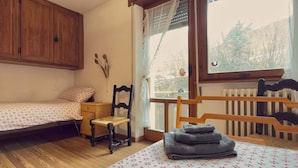 A small, cozy room with two single beds, a wooden chair, a small table, and a window with a view of trees. - Ca' Del Molin, spacious apartment with view (Cortina d'Ampezzo)