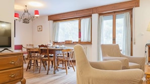 A dining area with a wooden table and chairs, a television, and a chandelier. - Ca' Del Molin, spacious apartment with view (Cortina d'Ampezzo)