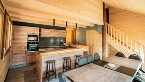 A modern kitchen with wooden cabinetry, a central island with stools, and a dining area with a table and chairs. - Large Duplex for 10 People At the Base of the Slopes & Bike Park • Garage & View (Châtel)