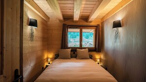 A cozy wooden room with a bed, two bedside lamps, a window with a view of buildings, and wooden walls. - Large Duplex for 10 People At the Base of the Slopes & Bike Park • Garage & View (Châtel)