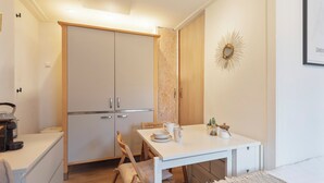 Una cocina pequeña con una mesa blanca, sillas y un armario.
