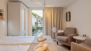 Habitación de hotel con cama, camilla de masaje, una silla, una mesita y un ventilador.