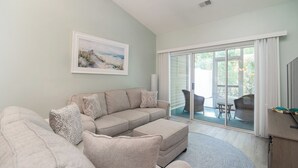 Una sala de estar con un sofá modular, un ventanal con vistas a muebles de exterior y un cuadro en la pared.