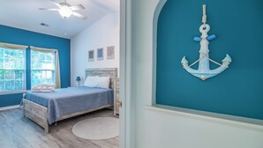 Un dormitorio con cama, ventilador de techo, ventana con cortinas y un adorno fijado a la pared.