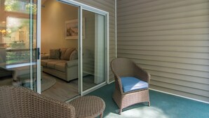 Un patio cubierto con mobiliario de mimbre, una puerta corrediza de vidrio que da a una sala de estar y vistas a la vegetación.