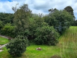 A lush garden with a variety of trees and shrubs, a stone bench, and a grassy area.